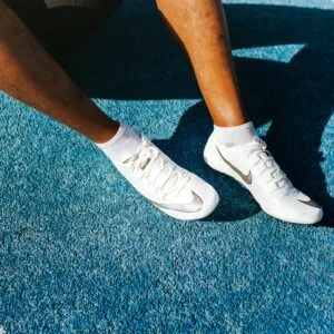 Close-up of an athlete's legs wearing Nike soccer cleats on a vibrant blue surface.